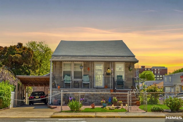 bungalow-style home with a fenced front yard, an attached carport, a gate, concrete driveway, and covered porch
