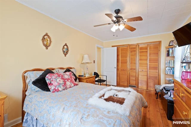 bedroom with crown molding, a ceiling fan, two closets, and hardwood / wood-style flooring