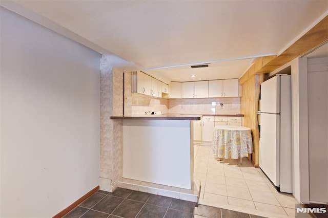 kitchen with visible vents, light tile patterned floors, white cabinets, freestanding refrigerator, and a peninsula