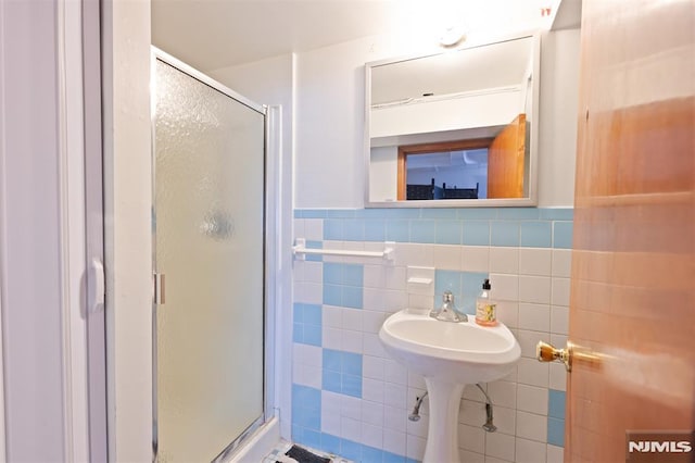 full bathroom with a wainscoted wall, tile walls, and a shower stall