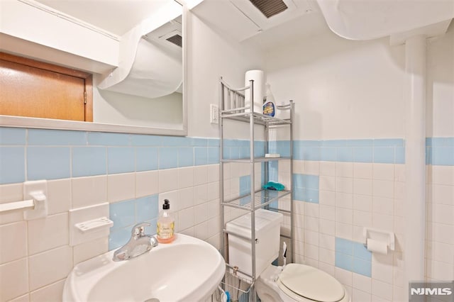 bathroom featuring a sink, toilet, a wainscoted wall, tile walls, and visible vents