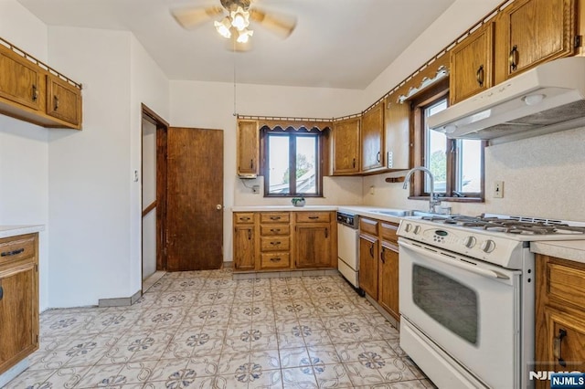 kitchen with white appliances, under cabinet range hood, brown cabinetry, and a sink