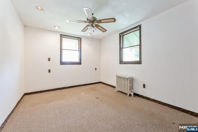 empty room with radiator heating unit, a wealth of natural light, and light carpet