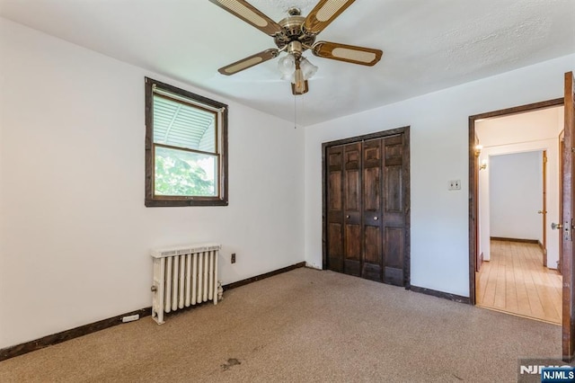 unfurnished bedroom featuring carpet floors, baseboards, radiator, and a closet