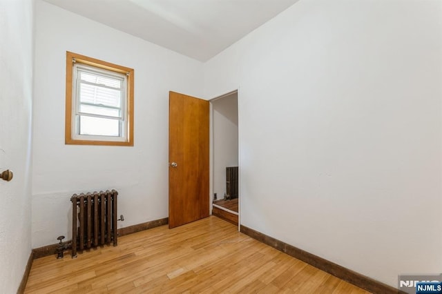 empty room with radiator heating unit, baseboards, and light wood-type flooring
