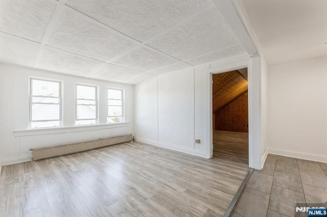 spare room with wood finished floors, baseboards, and a baseboard heating unit