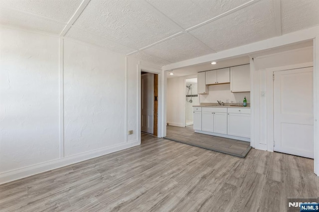 unfurnished living room featuring baseboards, a sink, and light wood-style flooring