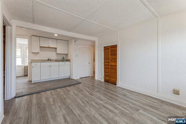 kitchen featuring radiator, baseboards, white cabinetry, and light wood finished floors