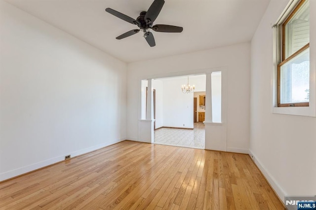 spare room with light wood-style floors, baseboards, and ceiling fan with notable chandelier