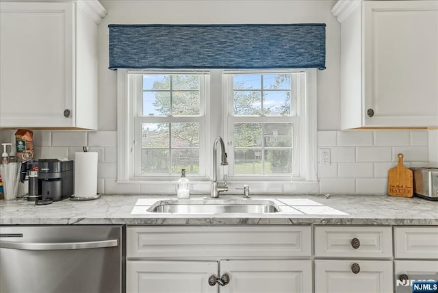 kitchen featuring stainless steel dishwasher, a sink, white cabinetry, and tasteful backsplash