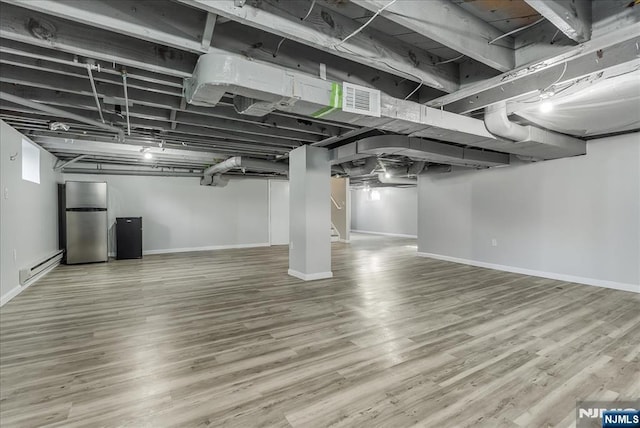 finished basement featuring visible vents, freestanding refrigerator, wood finished floors, baseboards, and baseboard heating