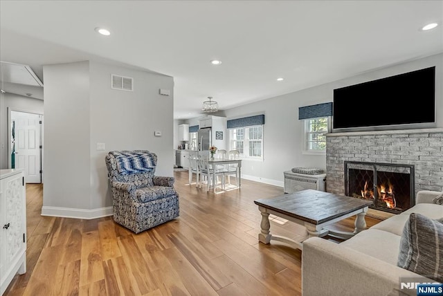 living room featuring visible vents, light wood-style flooring, baseboards, and a brick fireplace