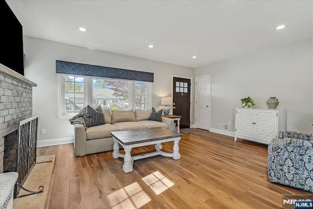 living area with light wood-style floors, baseboards, a brick fireplace, and recessed lighting