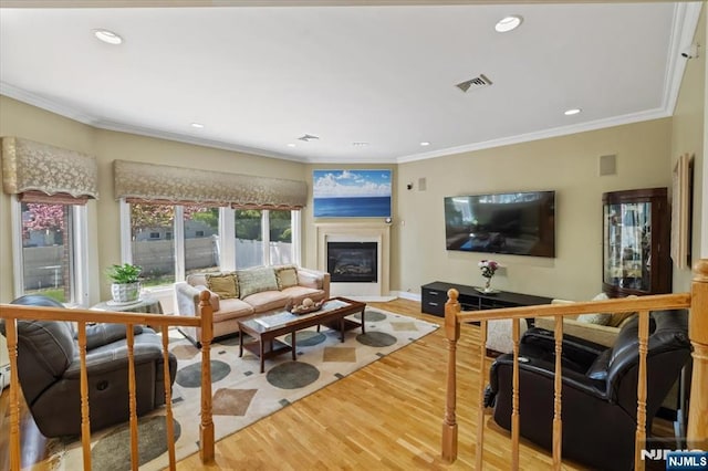 living room featuring visible vents, crown molding, a glass covered fireplace, and wood finished floors