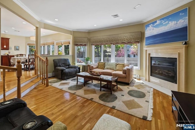 living room with visible vents, ornamental molding, a healthy amount of sunlight, a fireplace, and light wood-style flooring