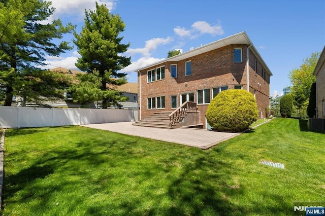 rear view of house featuring fence, central AC, brick siding, a patio, and a yard