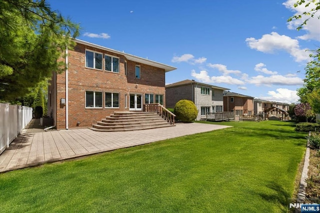 rear view of house with a lawn, brick siding, fence, a patio, and stairs