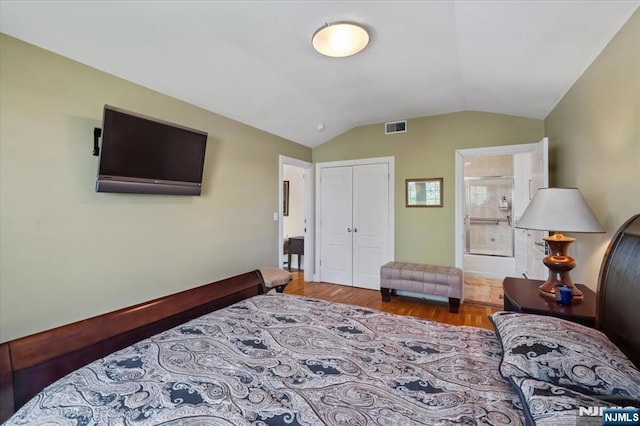 bedroom featuring visible vents, vaulted ceiling, wood finished floors, a closet, and ensuite bath