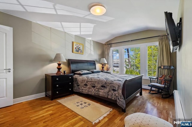 bedroom with baseboards, vaulted ceiling, a baseboard heating unit, and wood finished floors
