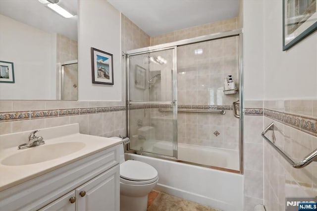 bathroom with vanity, tile patterned flooring, toilet, tile walls, and combined bath / shower with glass door