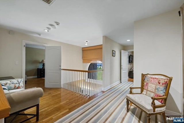 living area with baseboards, wood finished floors, visible vents, and an upstairs landing