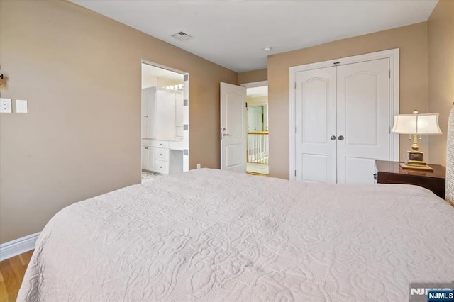 bedroom with ensuite bath, baseboards, wood finished floors, visible vents, and a closet