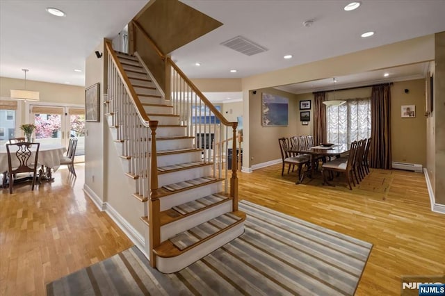 stairs with baseboards, baseboard heating, wood finished floors, and visible vents