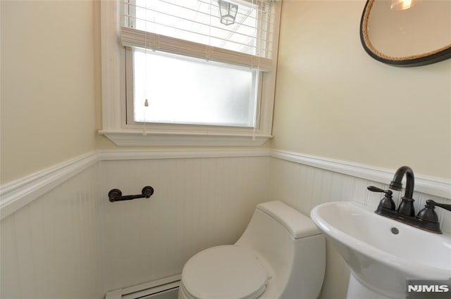 half bathroom with plenty of natural light, baseboard heating, a sink, a wainscoted wall, and toilet