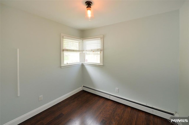 empty room featuring baseboards, baseboard heating, and dark wood-type flooring
