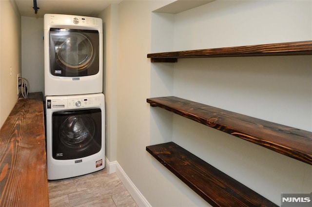 clothes washing area featuring stacked washer and dryer and baseboards