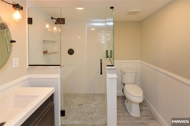 full bathroom with vanity, a wainscoted wall, toilet, and a shower stall
