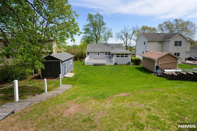 back of house featuring an outdoor structure, a yard, a wooden deck, and a shed