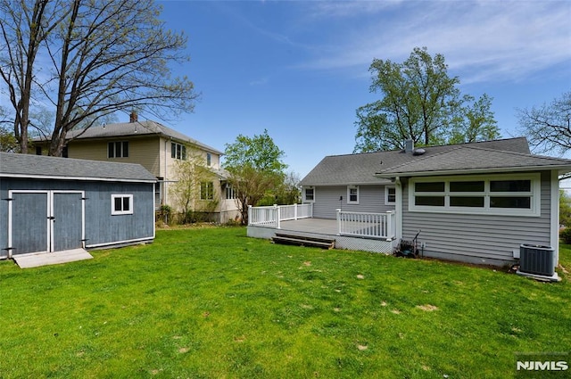 rear view of house with an outdoor structure, a deck, cooling unit, a storage unit, and a yard