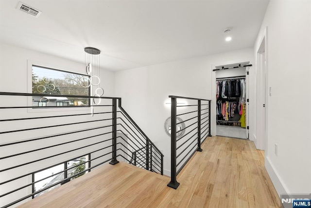 hallway featuring visible vents, light wood finished floors, baseboards, and an upstairs landing