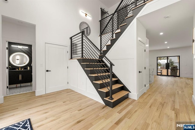 staircase featuring baseboards, recessed lighting, wood finished floors, and a towering ceiling