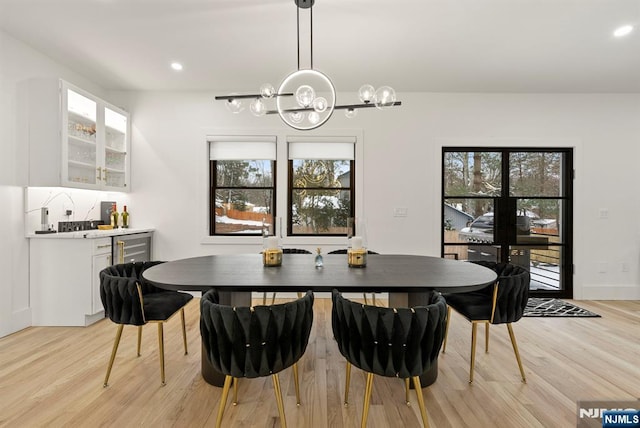 dining space with light wood-style floors, bar area, recessed lighting, and a notable chandelier