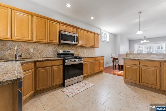 kitchen with light stone counters, a sink, appliances with stainless steel finishes, and backsplash