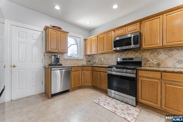 kitchen featuring brown cabinetry, appliances with stainless steel finishes, tasteful backsplash, a sink, and stone countertops