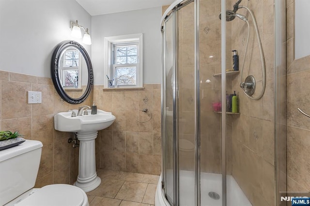 bathroom featuring tile patterned flooring, tile walls, toilet, and a shower stall