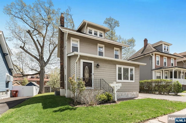 traditional style home with central air condition unit, a front lawn, fence, and a chimney