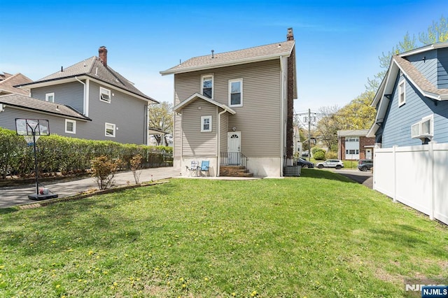 rear view of property featuring a lawn, fence, a chimney, and entry steps