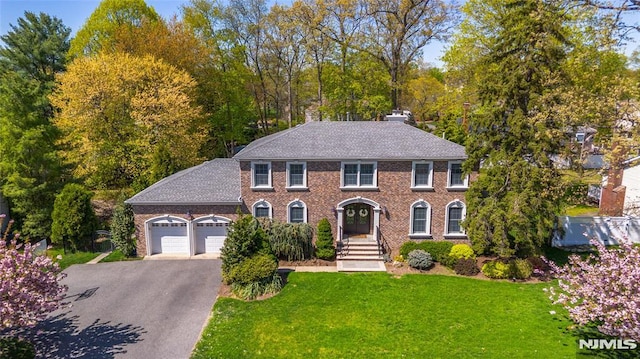 colonial home with brick siding, driveway, a front yard, and a garage