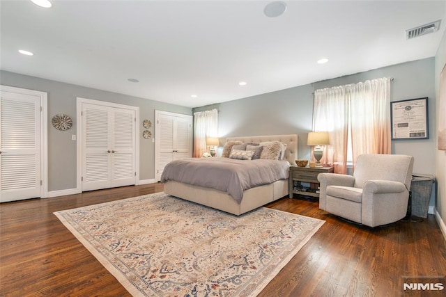 bedroom featuring baseboards, two closets, dark wood-style flooring, and visible vents
