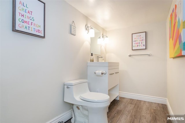 half bath with baseboards, vanity, toilet, and wood finished floors