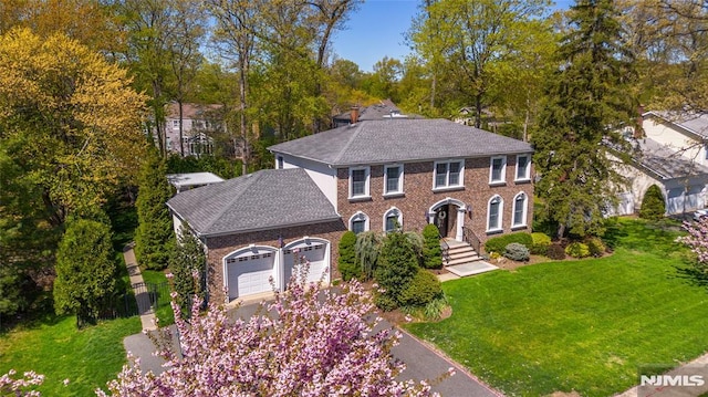 view of front of house featuring roof with shingles, brick siding, a garage, a front yard, and driveway