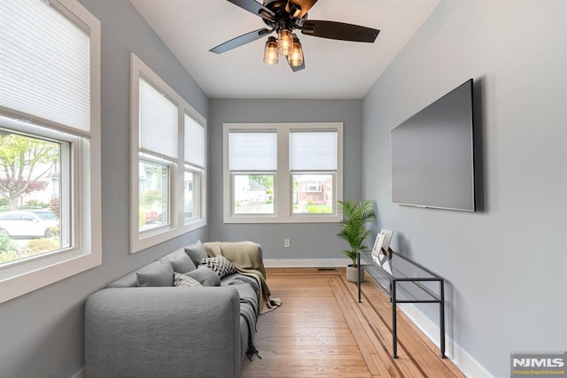 living area featuring light wood-style floors, baseboards, and a ceiling fan
