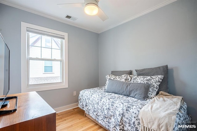 bedroom featuring visible vents, crown molding, baseboards, light wood-type flooring, and a ceiling fan