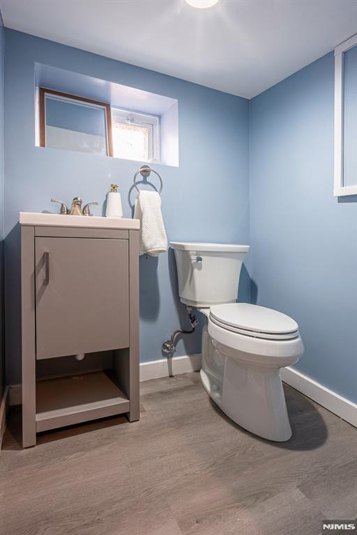 half bath featuring toilet, baseboards, wood finished floors, and vanity