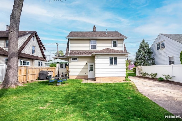 rear view of property featuring fence, a chimney, a lawn, and driveway