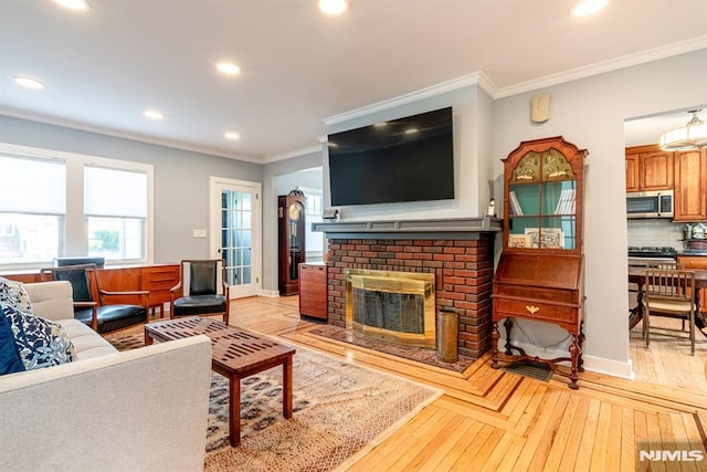 living room featuring recessed lighting, ornamental molding, light wood-style floors, and a brick fireplace